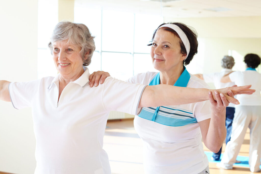 Portrait of sporty female supporting her friend while doing physical exercise in sport gym